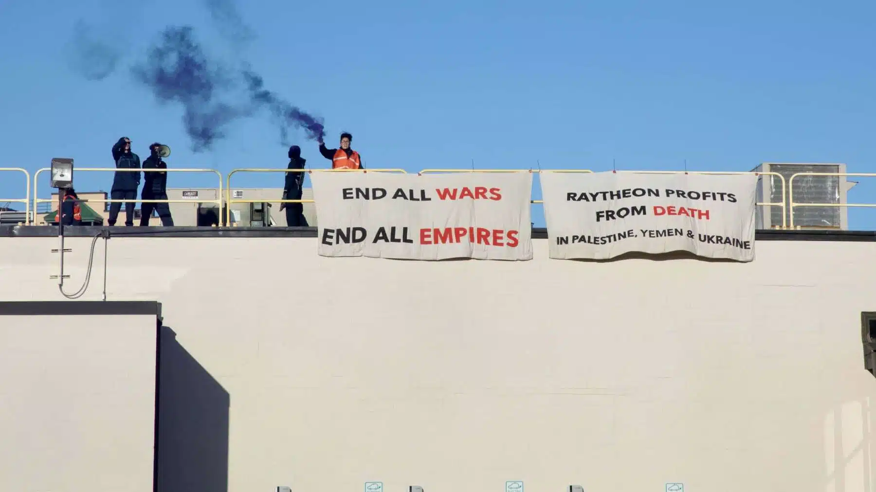 Activists climb onto the roof of Raytheon’s Cambridge facility in protest of war profiteering, killing of civilians