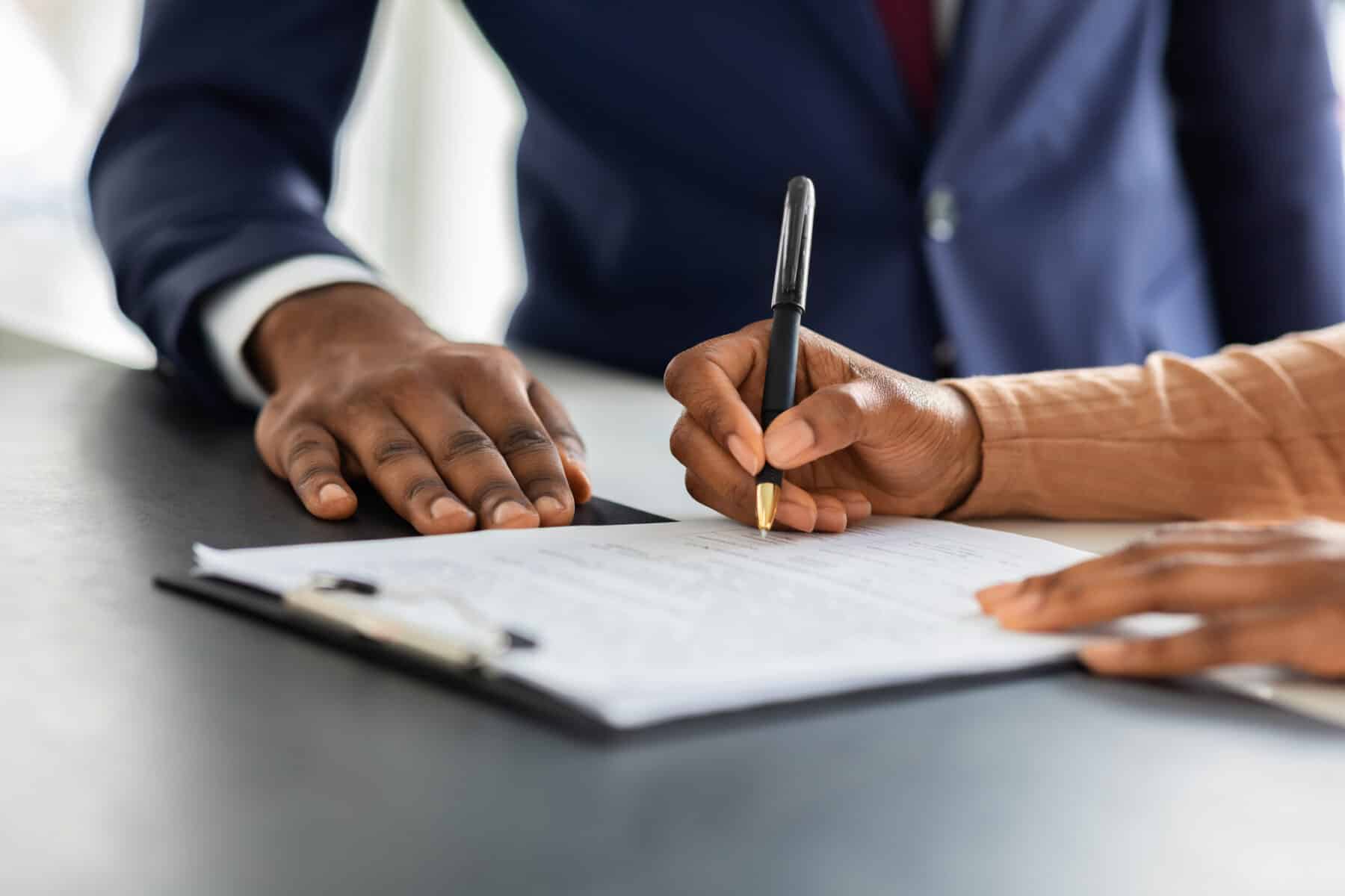 Two people signing contract, close-up of hands.