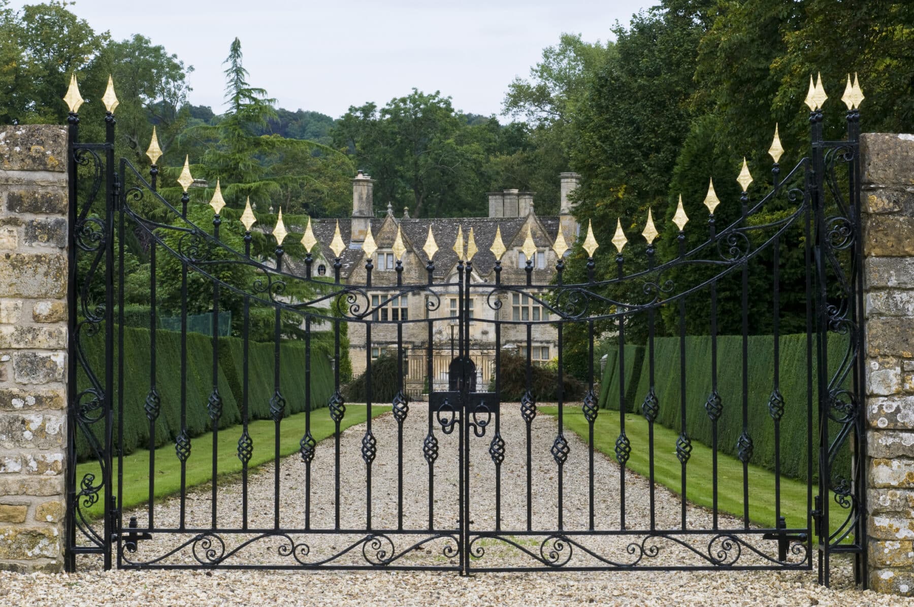 Ornate iron gate with historic manor house background.